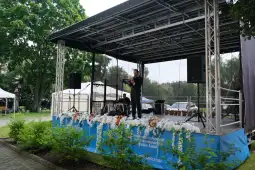Mężczyzna występuje na scenie, w tle kwiaty i sprzęt nagłaśniający.