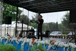 Mężczyzna w garniturze przemawia na scenie, w tle kwiaty i publiczność.