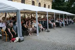 Grupa starszych osób siedzących pod namiotem na zewnątrz.