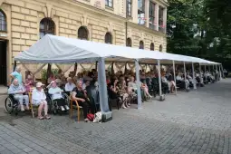Grupa seniorów siedzących pod dużym namiotem na zewnątrz.