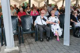 Grupa osób siedzących na krzesłach w plenerze, niektórzy z butelkami wody.