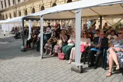 Grupa ludzi siedzących pod namiotami na zewnątrz, uczestniczących w wydarzeniu.