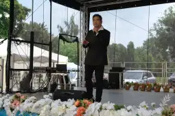 Mężczyzna w czarnym garniturze śpiewa na scenie, w tle dekoracje i sprzęt muzyczny.