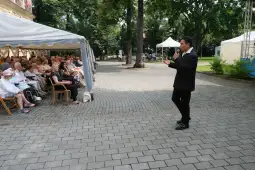 Mężczyzna w garniturze przemawia do zgromadzonej publiczności na świeżym powietrzu.