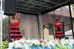 Tancerki w czerwonych strojach folklorystycznych tańczą na scenie.