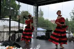 Tancerki w czerwono-czarnych strojach folklorystycznych tańczą na scenie.