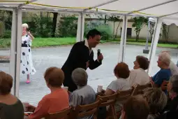 Mężczyzna w garniturze śpiewa dla grupy kobiet siedzących na krzesłach.