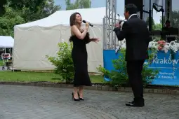 Dwoje wykonawców śpiewających na scenie podczas występu na świeżym powietrzu.
