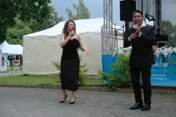 Dwoje wykonawców śpiewających na scenie podczas występu na świeżym powietrzu.