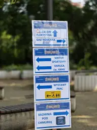 Tablice informacyjne z kierunkami do różnych miejsc, w tym gastronomii, sektora sportowego i toalety.