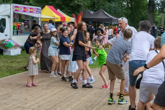 Grupa ludzi tańczących na festynie, dzieci i dorośli bawią się razem.