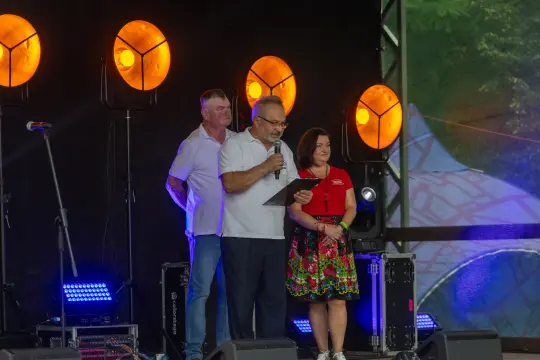 Trzech mówców na scenie podczas wydarzenia, jeden z nich trzyma mikrofon.