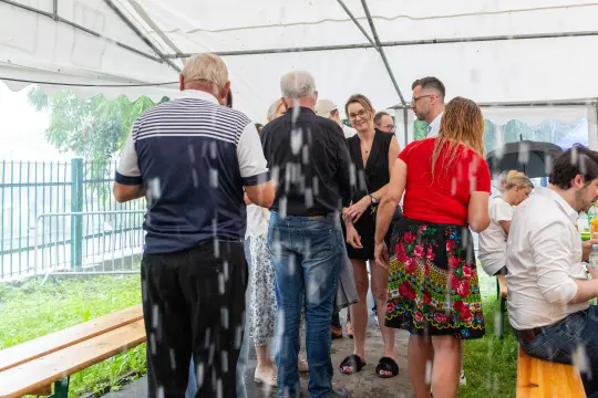 Grupa ludzi w namiocie podczas deszczu, rozmawiających i spędzających czas razem.