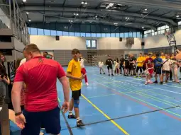 Grupa młodych ludzi w hali sportowej, przygotowująca się do rywalizacji.