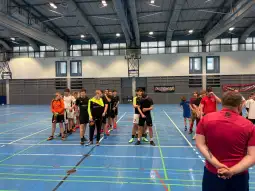 Grupa młodych sportowców w kolejce na trening w hali sportowej.
