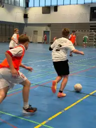 Młodzi zawodnicy grają w piłkę nożną na hali sportowej.