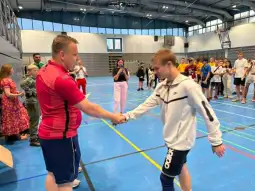 Młodzi sportowcy witają się na hali sportowej podczas wydarzenia.