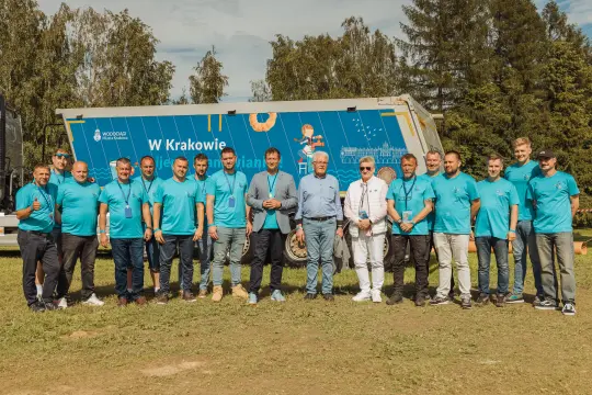 Grupa ludzi w niebieskich koszulkach na tle przyczepy w Krakowie.