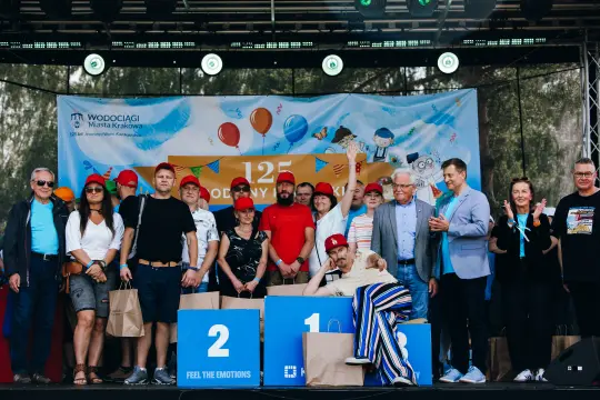 Grupa ludzi na scenie z nagrodami, świętujących 125-lecie Wodociągów Kraków.