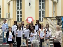Uczestnicy ceremonii wręczenia nagród, trzymający dyplomy i torby, stoją na schodach.