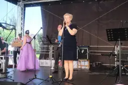 Kobieta w niebieskiej sukience przemawia do mikrofonu na scenie.