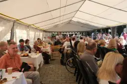 Spotkanie ludzi w namiocie, przy stołach z jedzeniem i napojami.