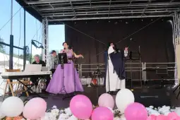 Występ artystów na scenie, z fortepianem i dekoracjami w różowych balonach.