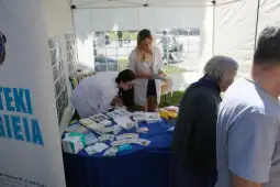 Kobiety przy stoisku informacyjnym, rozdające ulotki i materiały promocyjne.