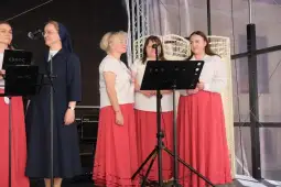 Cztery kobiety w tradycyjnych strojach ludowych stoją przy mikrofonie na scenie.