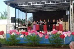 Grupa osób śpiewających na scenie, w strojach ludowych, z instrumentami muzycznymi.