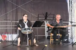Muzycy grający na scenie, jeden na gitarze, drugi na perkusji.