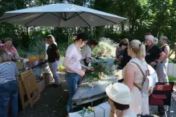 Grupa kobiet tworzy kompozycje kwiatowe w ogrodzie.