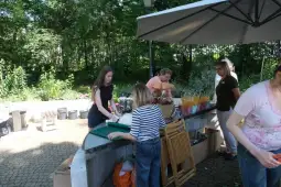 Kobiety przygotowujące kwiaty i dekoracje na zewnątrz, w otoczeniu zieleni.