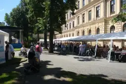 Tłum ludzi w wózkach inwalidzkich pod namiotami przy budynku.