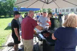 Grillowanie kiełbasek podczas letniego pikniku z uczestnikami w tle.