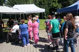 Grupa osób w różnych strojach, w tym pracowników medycznych, w kolejce do stoiska.