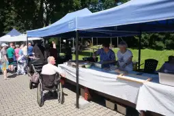 Kolejka do stoiska z jedzeniem na festynie, osoby w różnym wieku, namioty w tle.