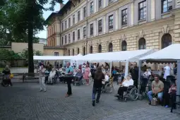 Spotkanie osób starszych w ogrodzie, z namiotami i uczestnikami w wózkach inwalidzkich.