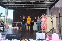 Grupa osób na scenie podczas wydarzenia, jedna z nich trzyma mikrofon.