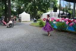 Kobieta w fioletowej sukni tańczy na tle festiwalu z dekoracjami i publicznością.