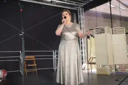 Kobieta w srebrnej sukni śpiewa na scenie.