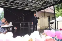 Mężczyzna w garniturze śpiewa na scenie, obok kobieta gra na pianinie. W tle dekoracje z balonów.