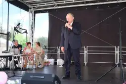 Mężczyzna przemawia do publiczności na scenie, obok siedzą kobiety i sprzęt muzyczny.