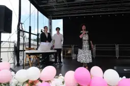 Kobieta śpiewa na scenie, obok dwóch osób przy fortepianie, w tle dekoracje z balonów.