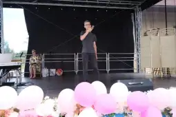 Chłopak występujący na scenie, obok siedząca kobieta, dekoracje w różowych kolorach.