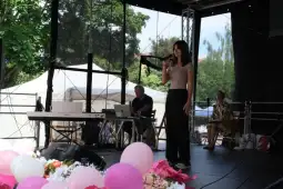 Młoda kobieta śpiewa na scenie, obok muzycy i publiczność w tle.