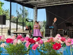 Występ artystów na scenie, kwiaty i dekoracje w tle.