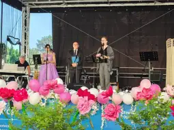 Występ artystyczny na scenie z muzykami i kwiatową dekoracją.