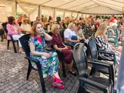 Grupa osób siedzących na krzesłach w namiocie, uczestniczących w wydarzeniu.