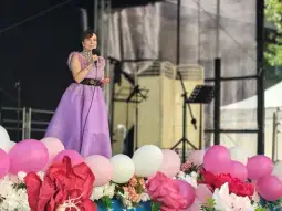 Kobieta w fioletowej sukni występuje na scenie, otoczona balonami i kwiatami.